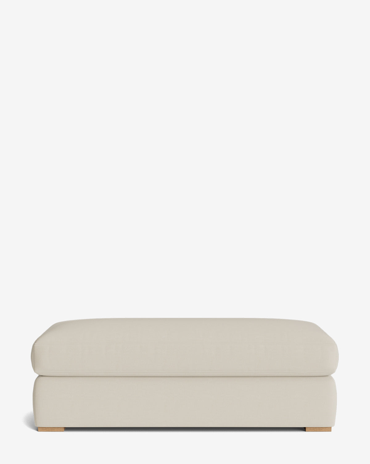 The Macy Upholstered Ottoman is a large, rectangular ottoman with rounded edges and low wooden feet, ideal as versatile living room furniture, shown against a plain white background, by Vendixs