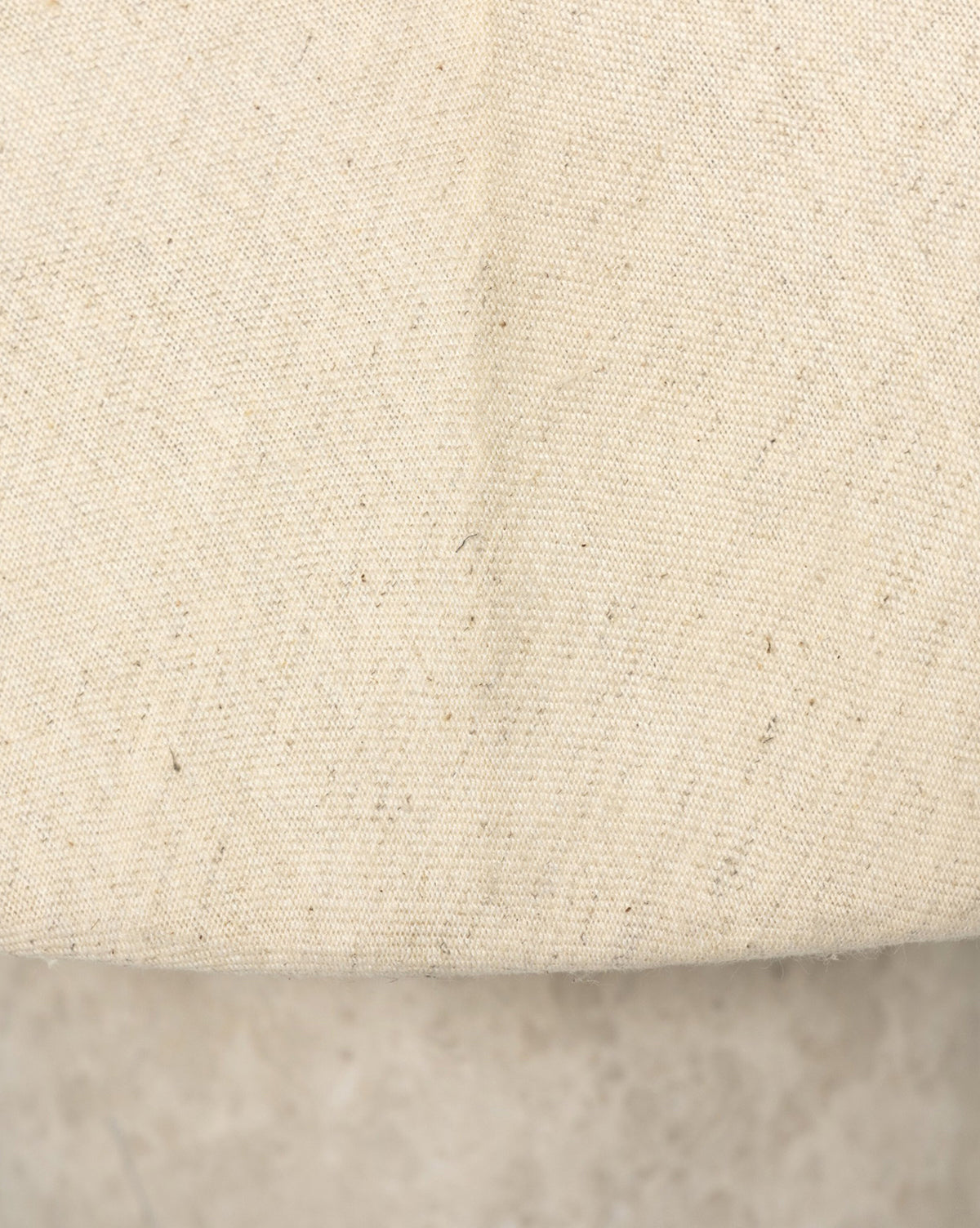 Close-up of the Malinska Table Lamps beige linen dome shade, featuring a visible center seam, coarse texture with scattered dark fibers, and a curved edge that reveals its gray concrete base, by Vendixs