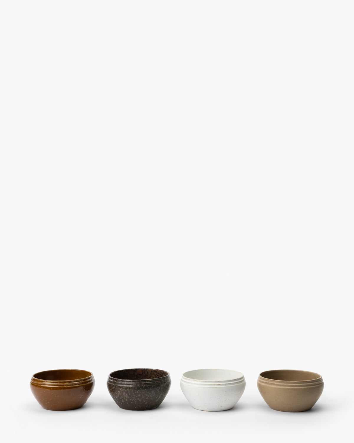 The Mariella Stoneware Bowls (Set of 4) features small, round bowls in brown, dark speckled, white speckled, and beige, displayed in a row on a white background to highlight their organic texture and handmade quality by Vendixs