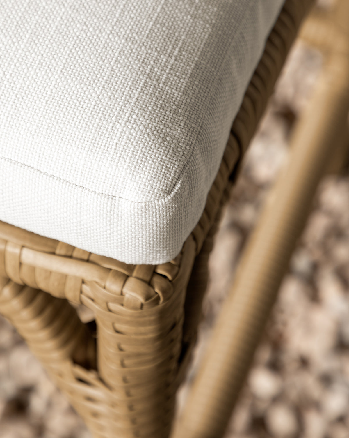 Close-up of the Makerspalm Marisol Indoor/Outdoor Counter Stool (Set of 2), featuring handwoven wicker and a light textured cushion, shown with a blurred pebble background. Vendixs
