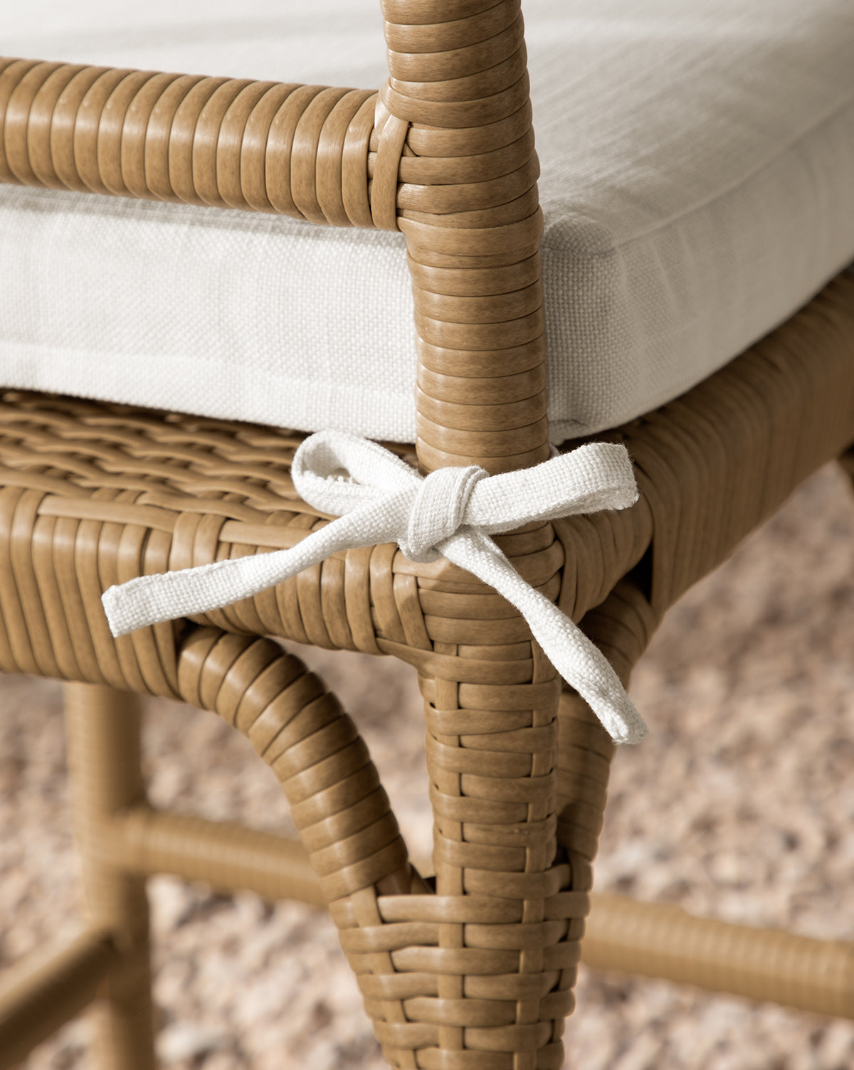 Close-up of the Makerspalm Marisol Indoor/Outdoor Counter Stool (Set of 2), featuring handwoven wicker, a white seat cushion secured with a fabric bow, and set on a textured beige carpet. Vendixs