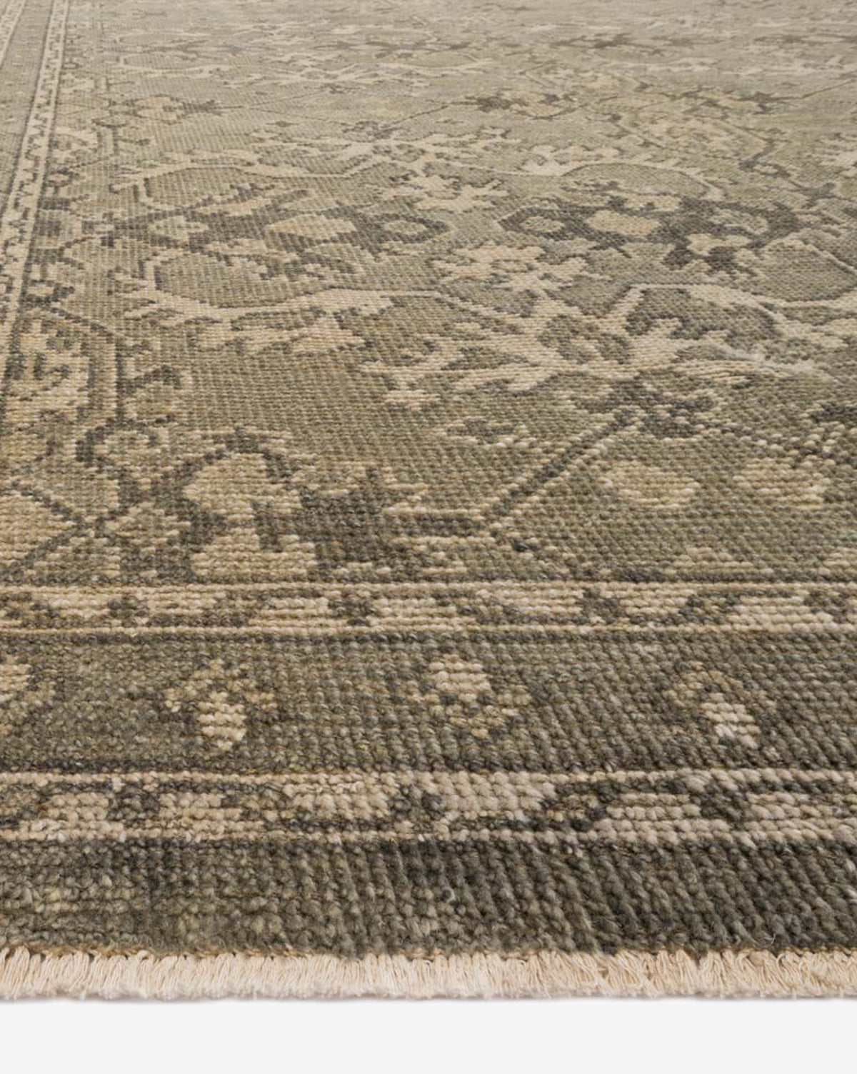A close-up of the Marola Hand-Knotted Wool Rug shows its durable, intricate faded floral and geometric patterns in muted green, beige, and brown hues, with a visible border and fringed edge, by Vendixs