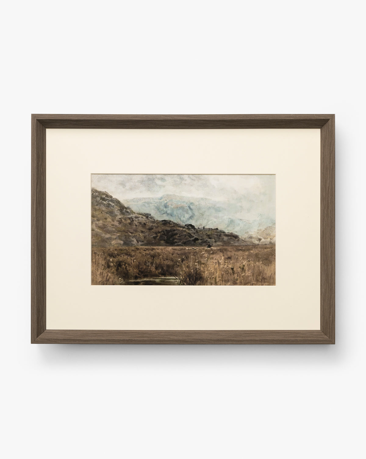 Marshland is a framed landscape painting with muted earthy tones, showing grassy hills and marshland beneath a cloudy sky. It features a simple, modern walnut woodgrain frame with a white mat for a soft, natural look by Vendixs