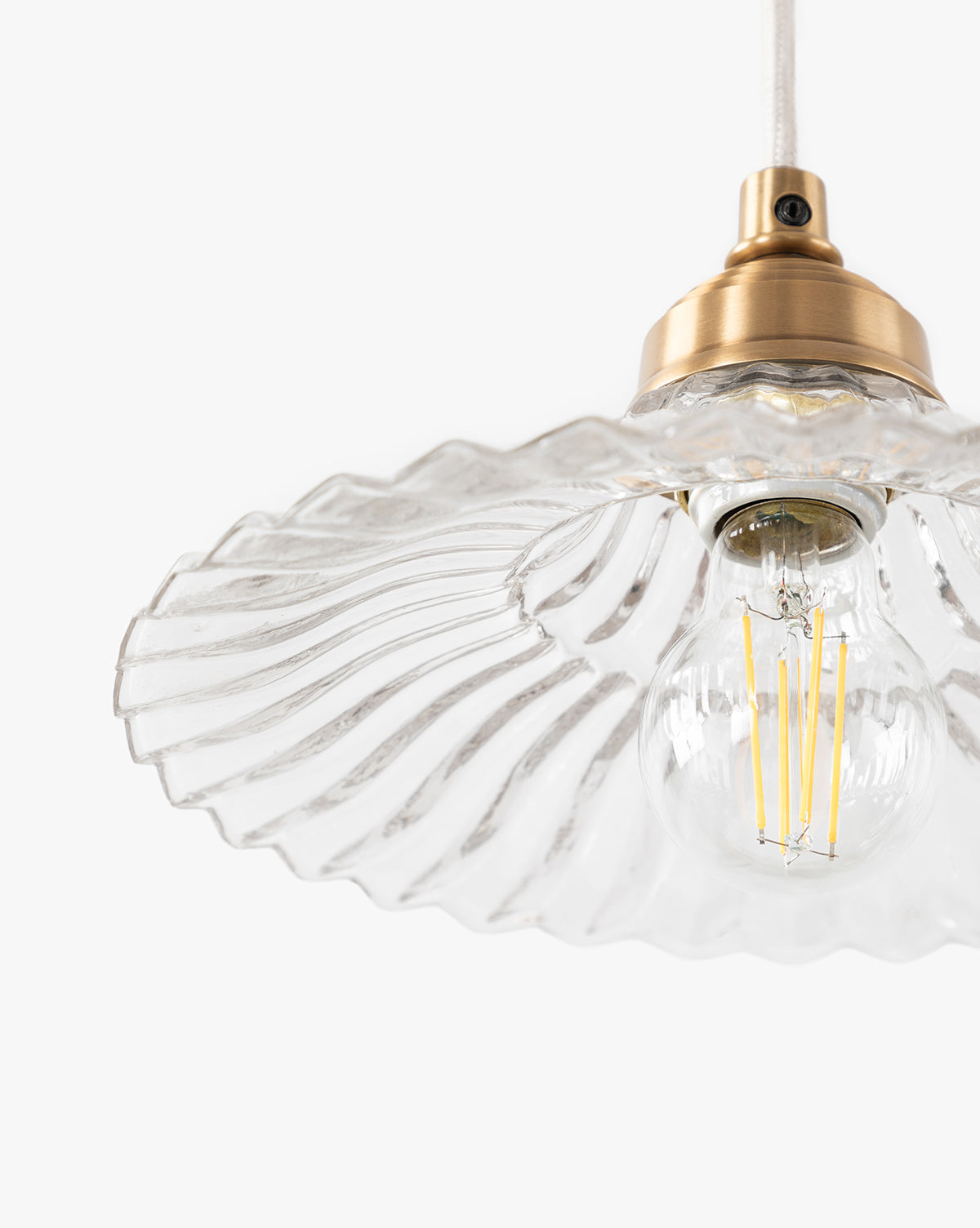 A close-up of the Vendixs x Loeffler Randall Maude Glass Pendant, showcasing its clear wavy glass shade, vintage-style exposed filament bulb, and elegant brass hardware set against a plain white background, by Vendixs