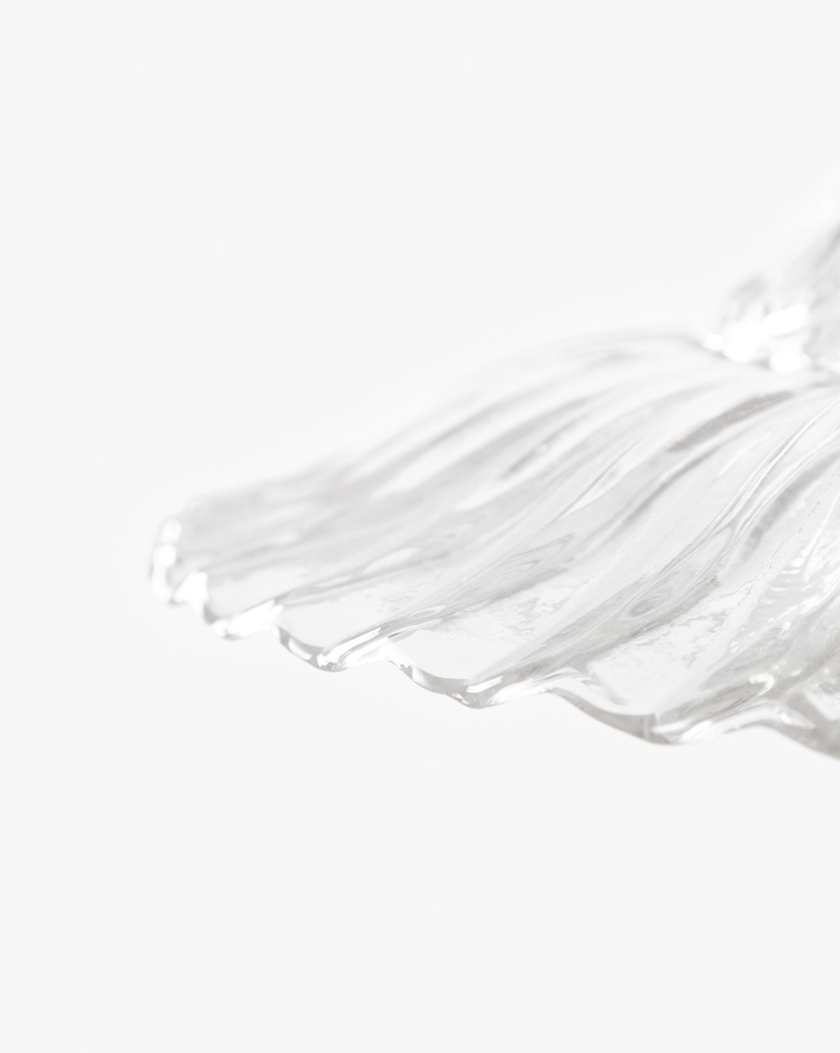 Close-up of a transparent, wavy glass shade with smooth lines on a white background. Its sculpted edge recalls the Vendixs x Loeffler Randall Maude Glass Pendant, ideal for bringing elegance to any space by Vendixs