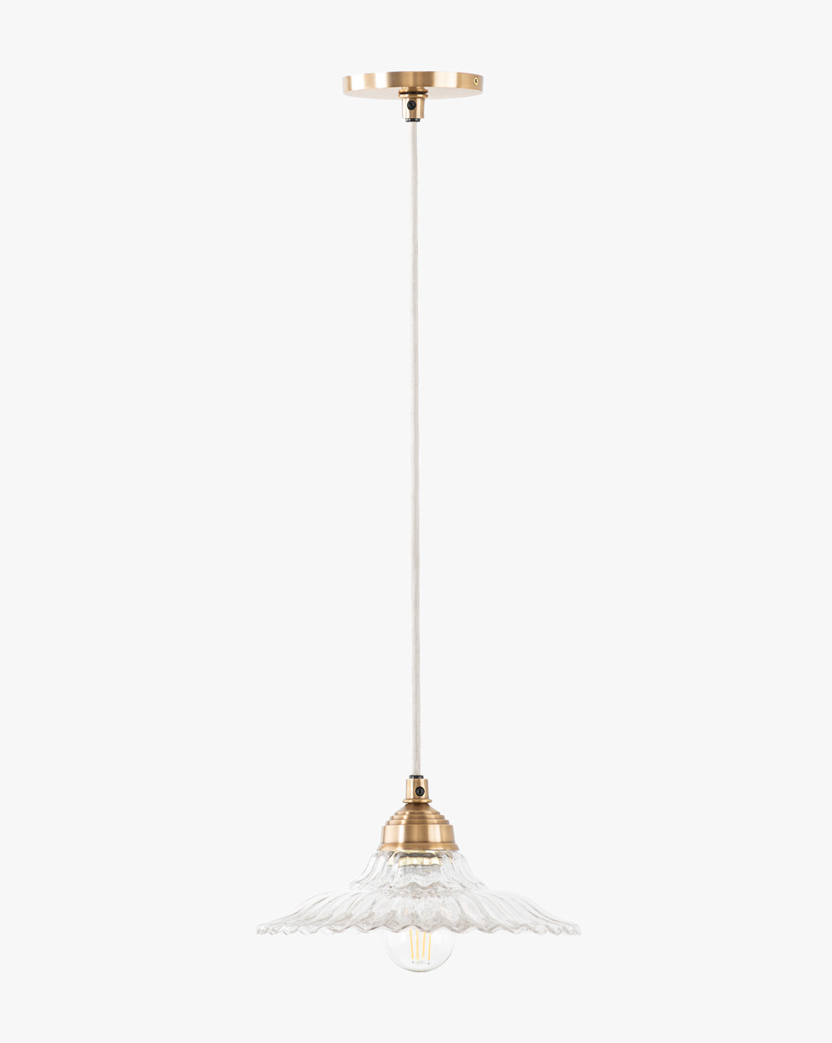 The Vendixs x Loeffler Randall Maude Glass Pendant features brass hardware, a white cord, and a clear scalloped glass shade that beautifully displays an exposed bulb, by McGee & Co.