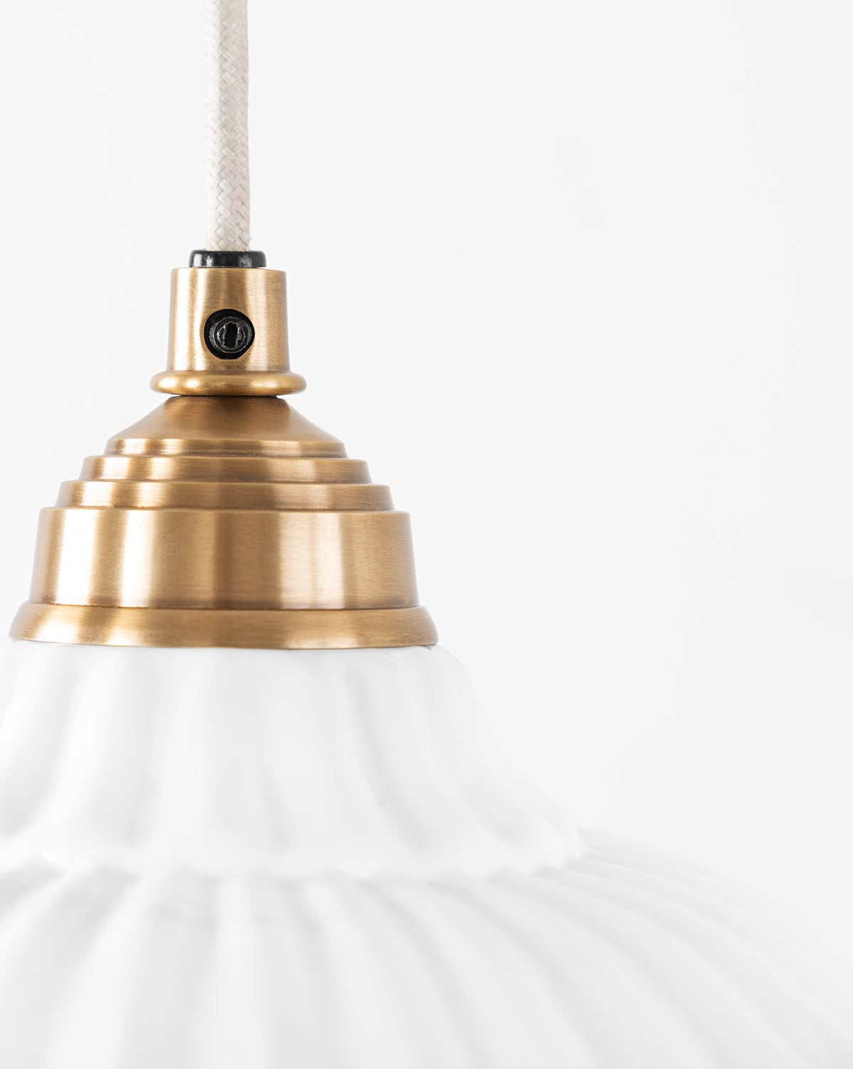 Close-up of the Vendixs x Loeffler Randall Maude Glass Pendant, showcasing its ribbed white glass shade and brass hardware, hanging by a white cord against a plain white background, by Vendixs
