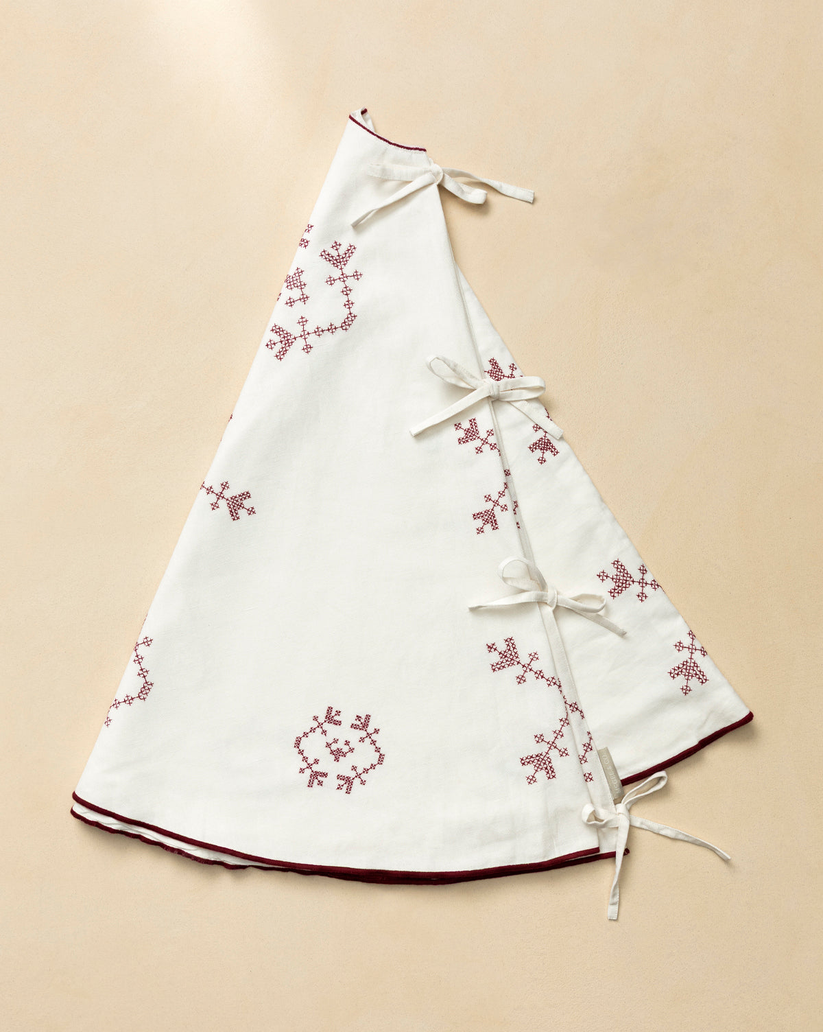 The McCallister Tree Skirt is a white, triangular vintage piece with red embroidered snowflakes, maroon trim, and four white ribbon ties—perfect for bringing heirloom charm to your holiday decor, by Vendixs