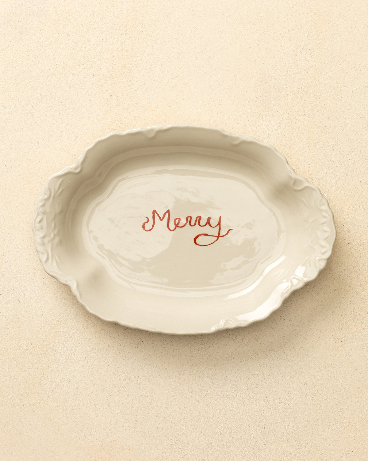 The Merry Stoneware Scalloped Platter is an oval white platter with decorative edges and "Merry" in red script at the center, perfect for holiday serving and festive table decor, by Vendixs