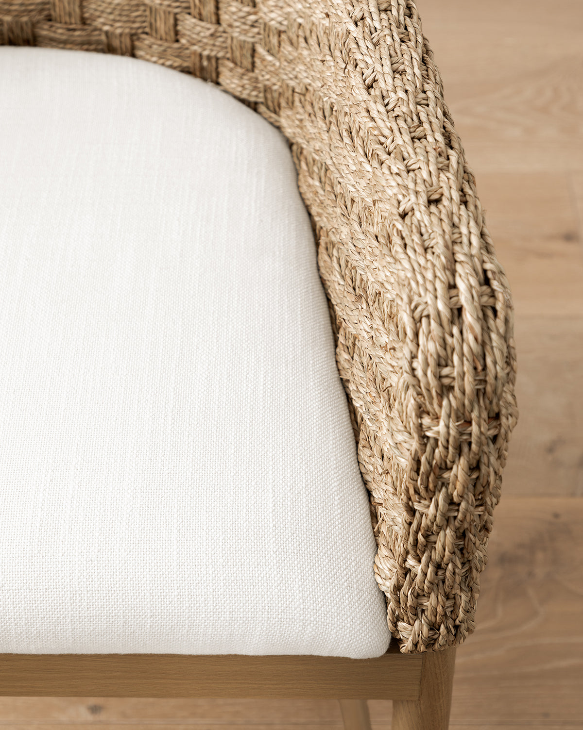 Close-up of the Molly Arm Chair, a modern seat with textured woven rattan armrests and a light beige fabric cushion, shown on a light wooden floor, by McGee & Co.