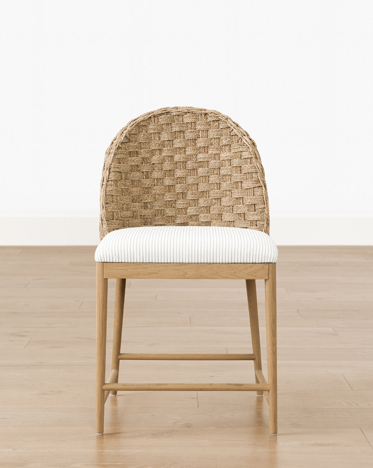 The Makerspalm Molly Dining Chair showcases a solid oak frame, woven rattan backrest, and striped cushioned seat, elegantly placed on a light wood floor against a plain white wall. Vendixs