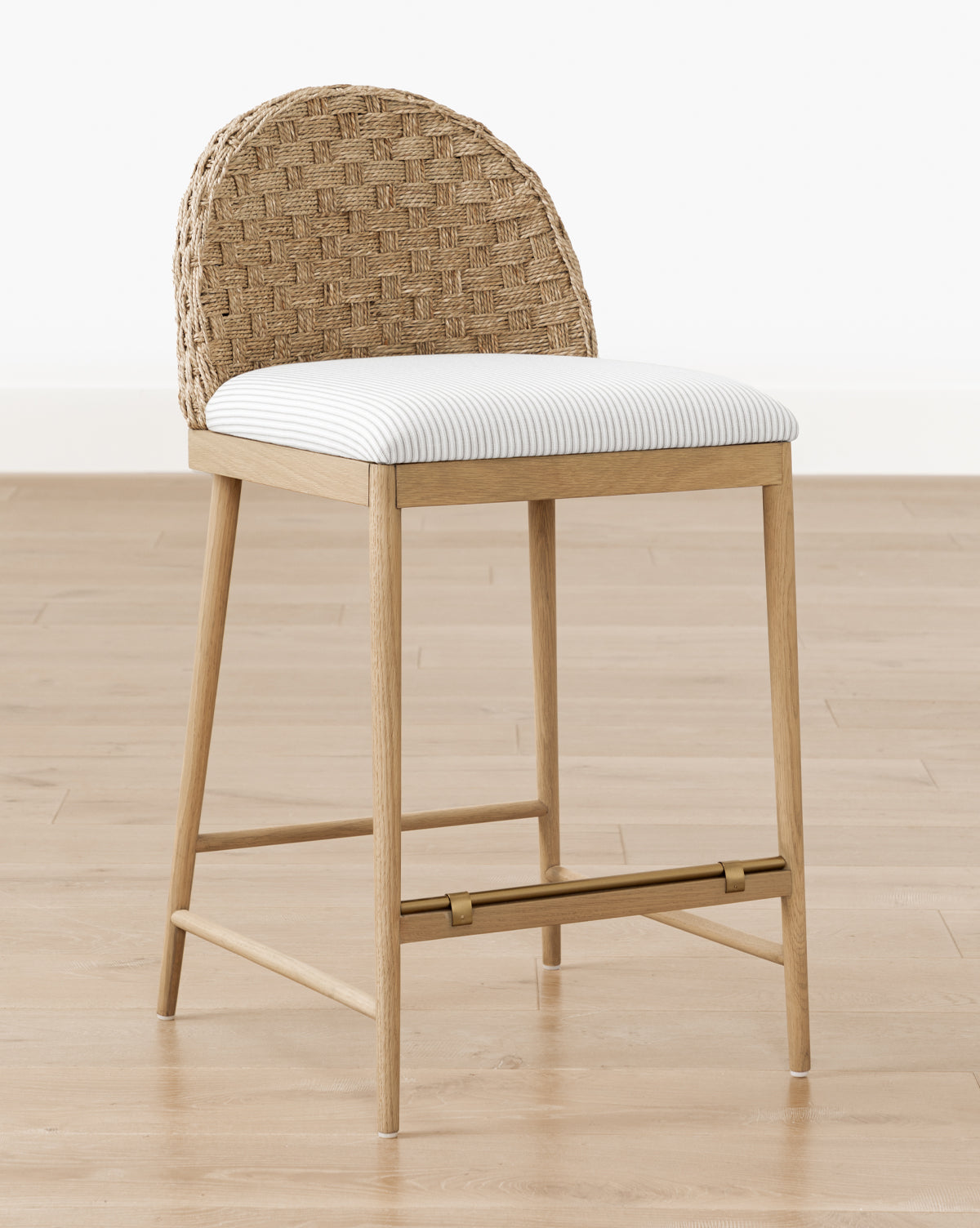 The Molly Stool, crafted from solid oak, features a natural finish, a woven rattan curved backrest, and a white cushioned seat, by Vendixs It is shown on a light wood floor against a plain white wall.