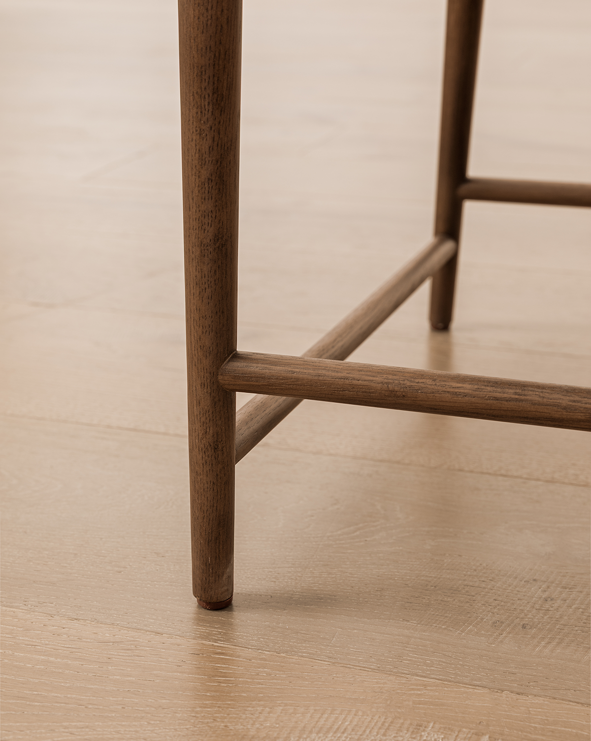 Close-up of the Molly Dining Chair leg with a horizontal support bar on a light wood floor, highlighting its simple, clean lines and natural solid oak texture, by Vendixs