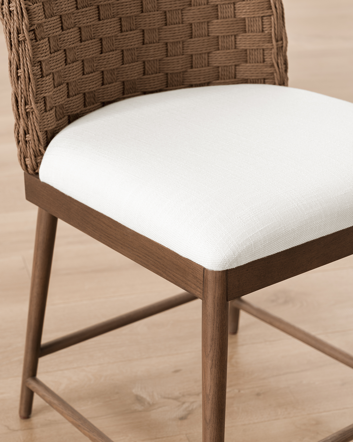 The Molly Dining Chair features a woven brown backrest, white cushioned seat, and solid oak legs, shown here on a light wood floor, by Vendixs