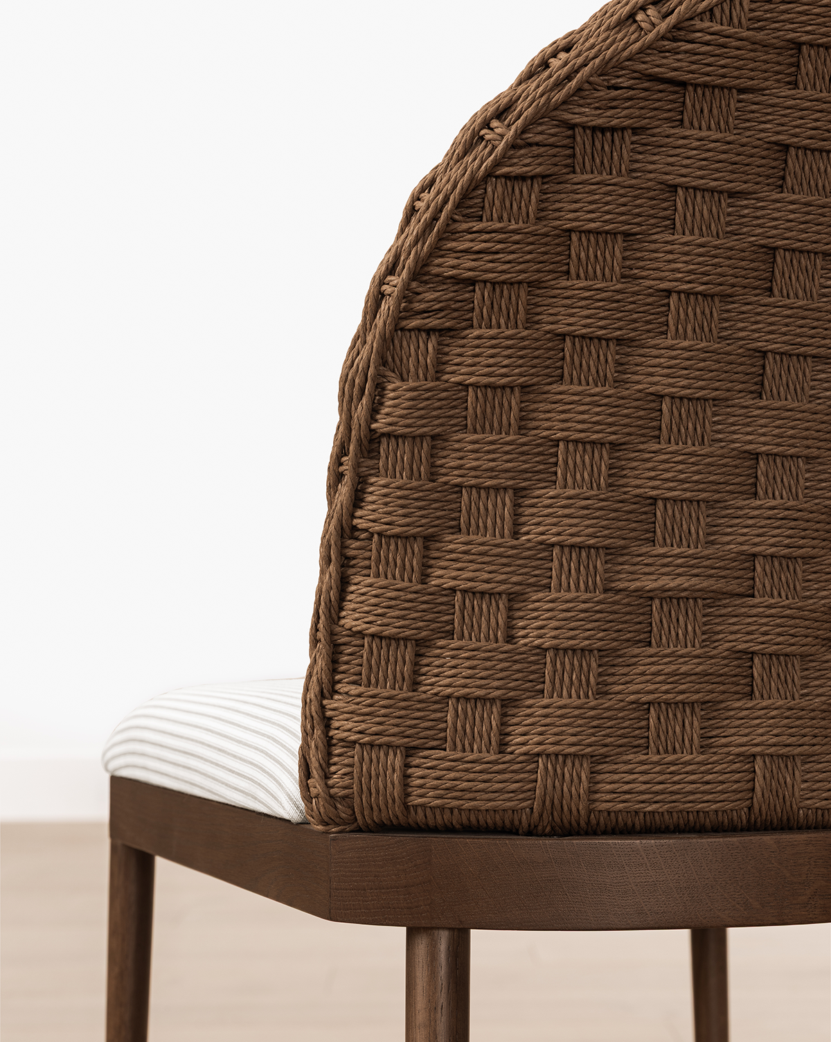 A close-up of the Molly Stool, showcasing its curved, woven brown backrest and white striped cushioned seat on solid oak legs, set against a light floor and white wall, by Vendixs