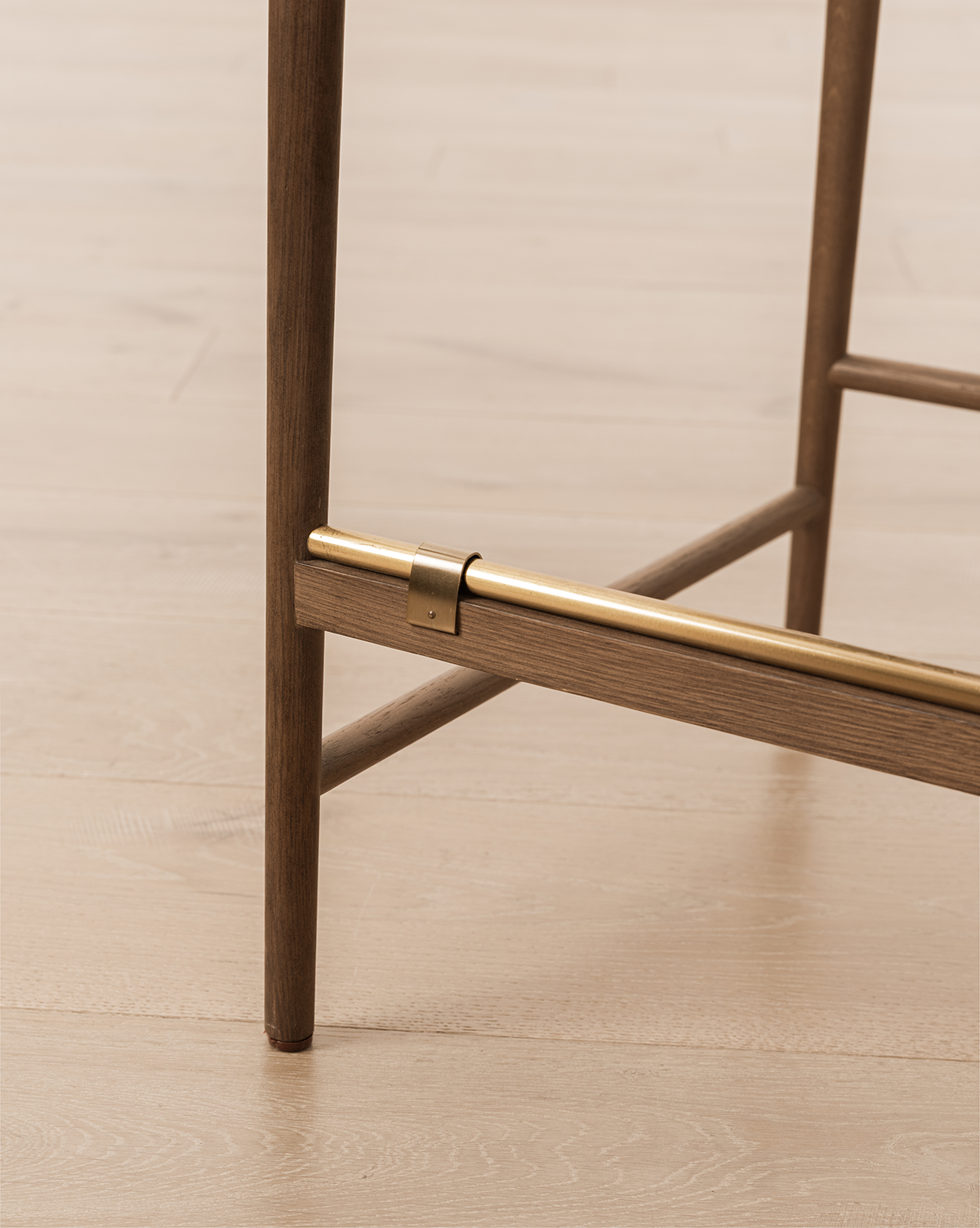 Close-up of the Molly Stool’s solid oak leg with a brass footrest near the base on a light wood floor—perfect refined detailing for this natural bar or counter stool, by Vendixs