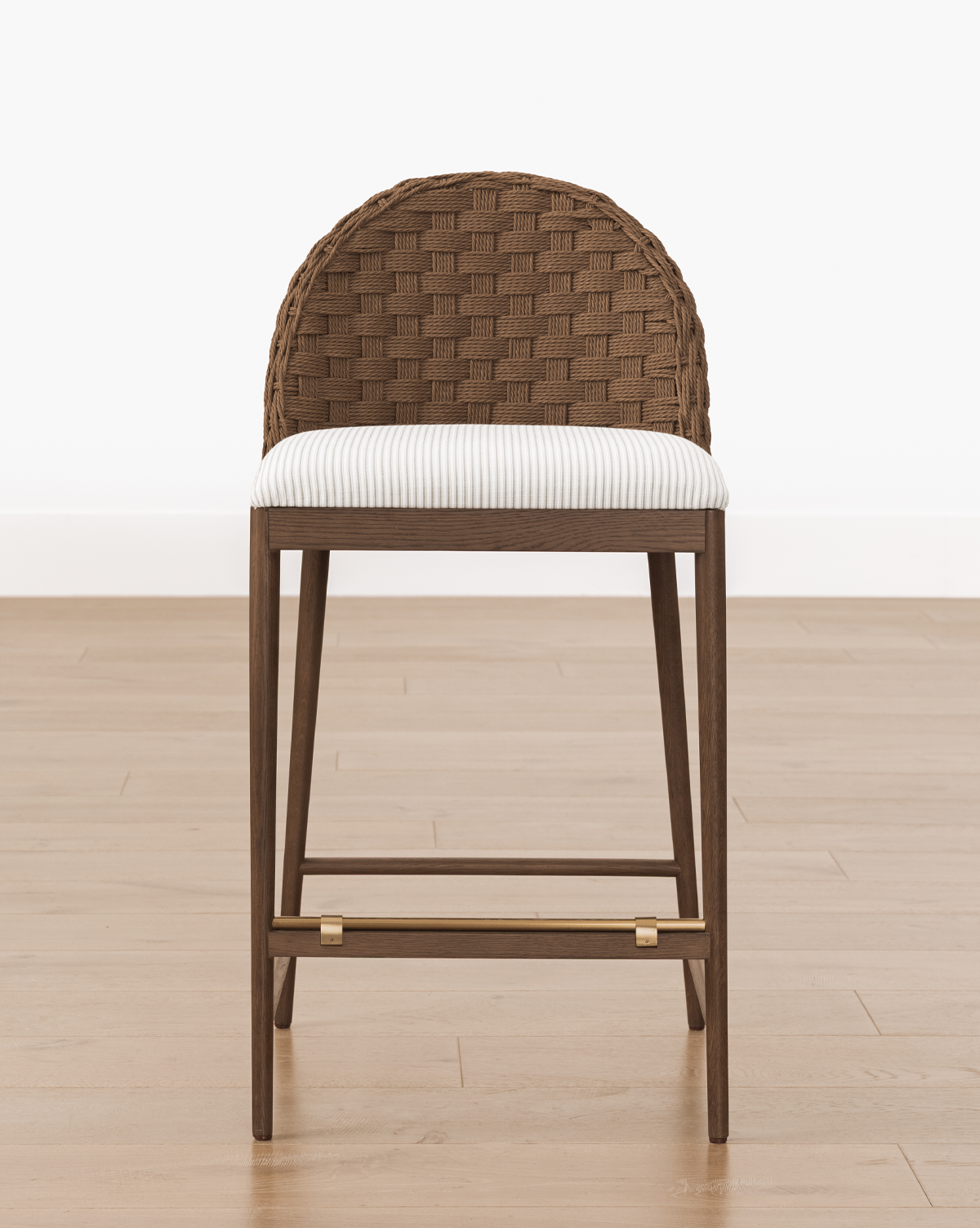 The Molly Stool features a woven brown curved backrest, striped cushioned seat, and solid oak legs with gold accents, standing on a light wood floor against a white background, by Vendixs