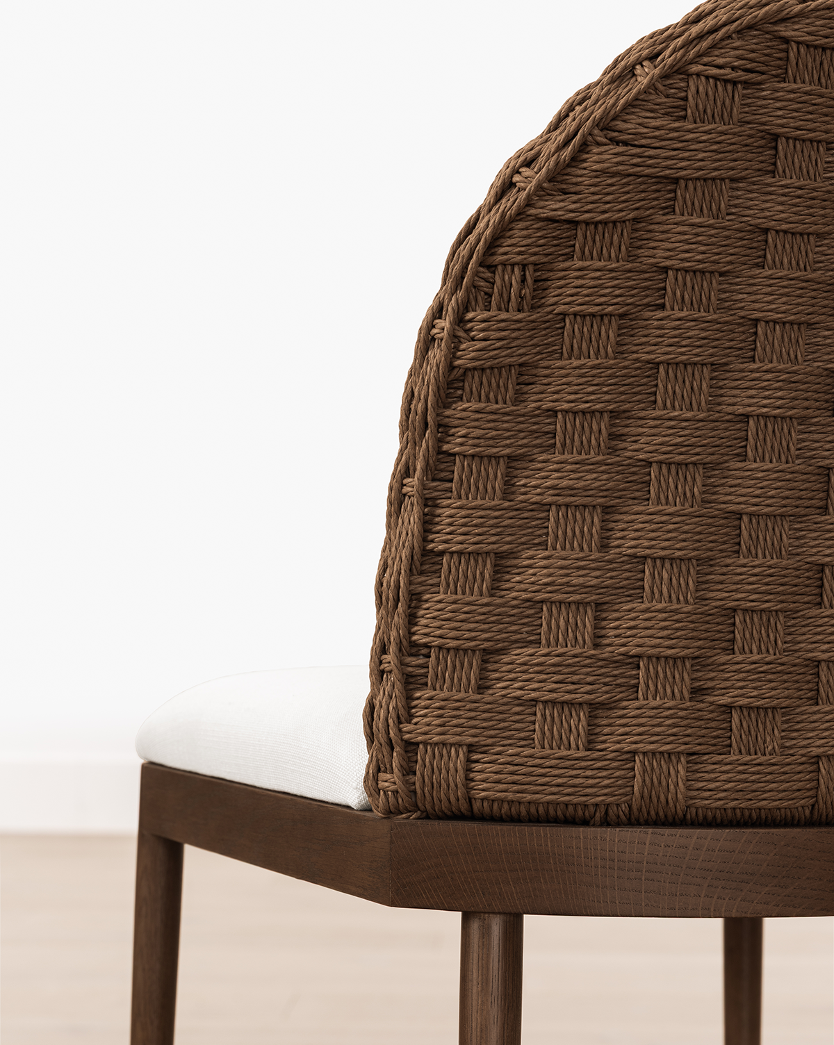 A close-up of the Molly Stool, featuring a solid oak frame, brown woven backrest, and white cushioned seat, set against a plain white wall and light wood floor, by Vendixs