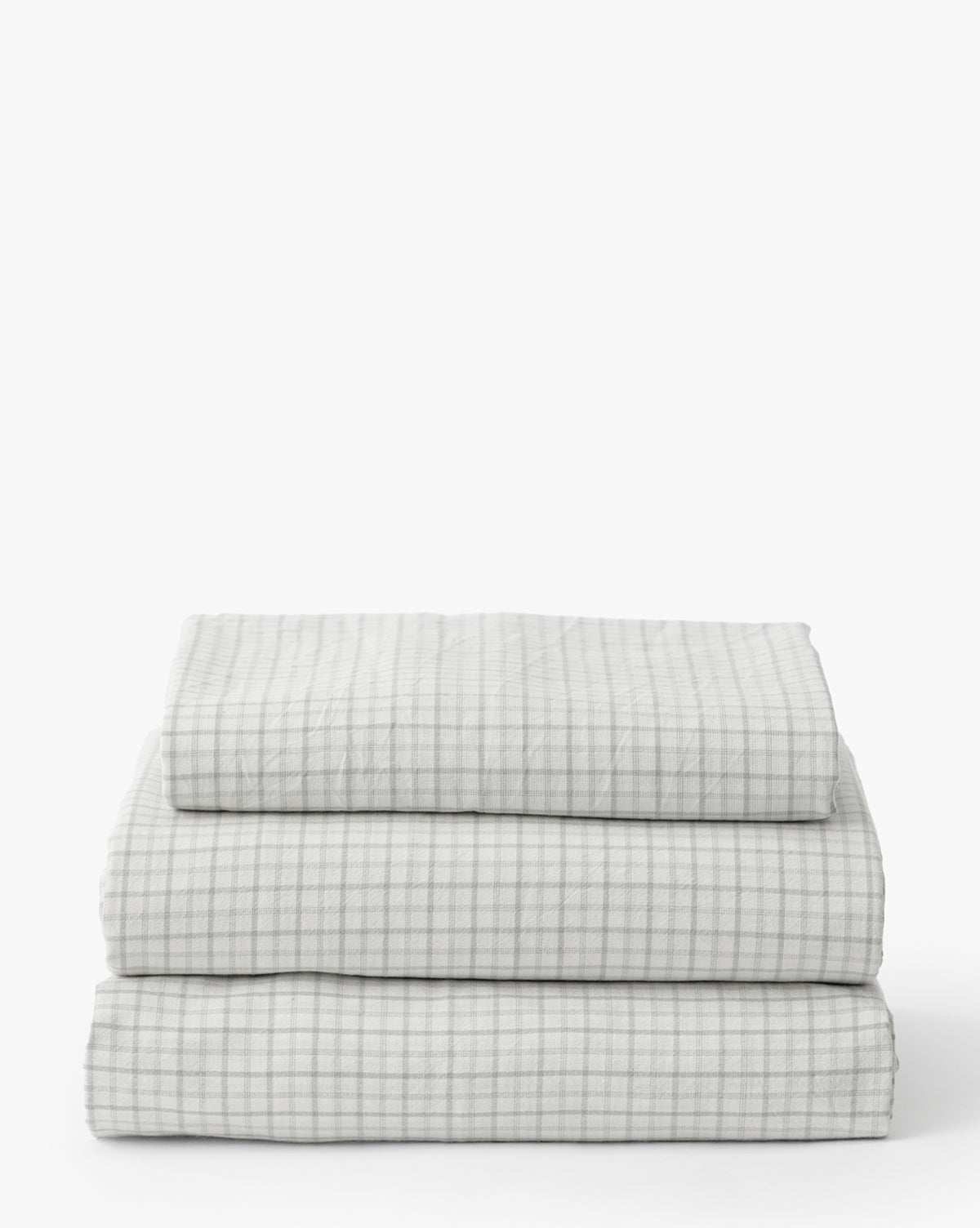 The Nell Blue Twin Kids Sheet Set includes three neatly folded white cotton sheets with a subtle light gray checkered pattern, ideal for plaid bedding, shown against a plain white background by McGee & Co.
