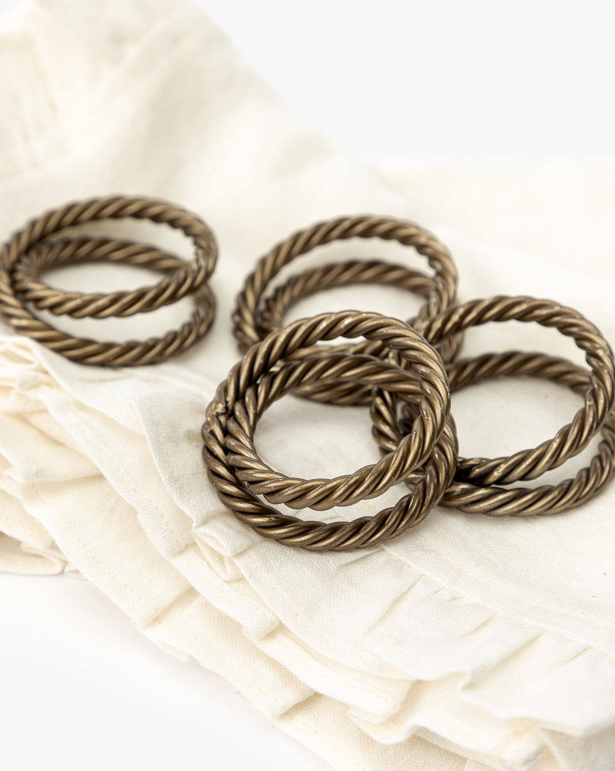 A set of four Nichols Napkin Rings sits atop folded cream-colored, ruffle-edged napkins, creating an elegant table setting against a simple white background, by Vendixs