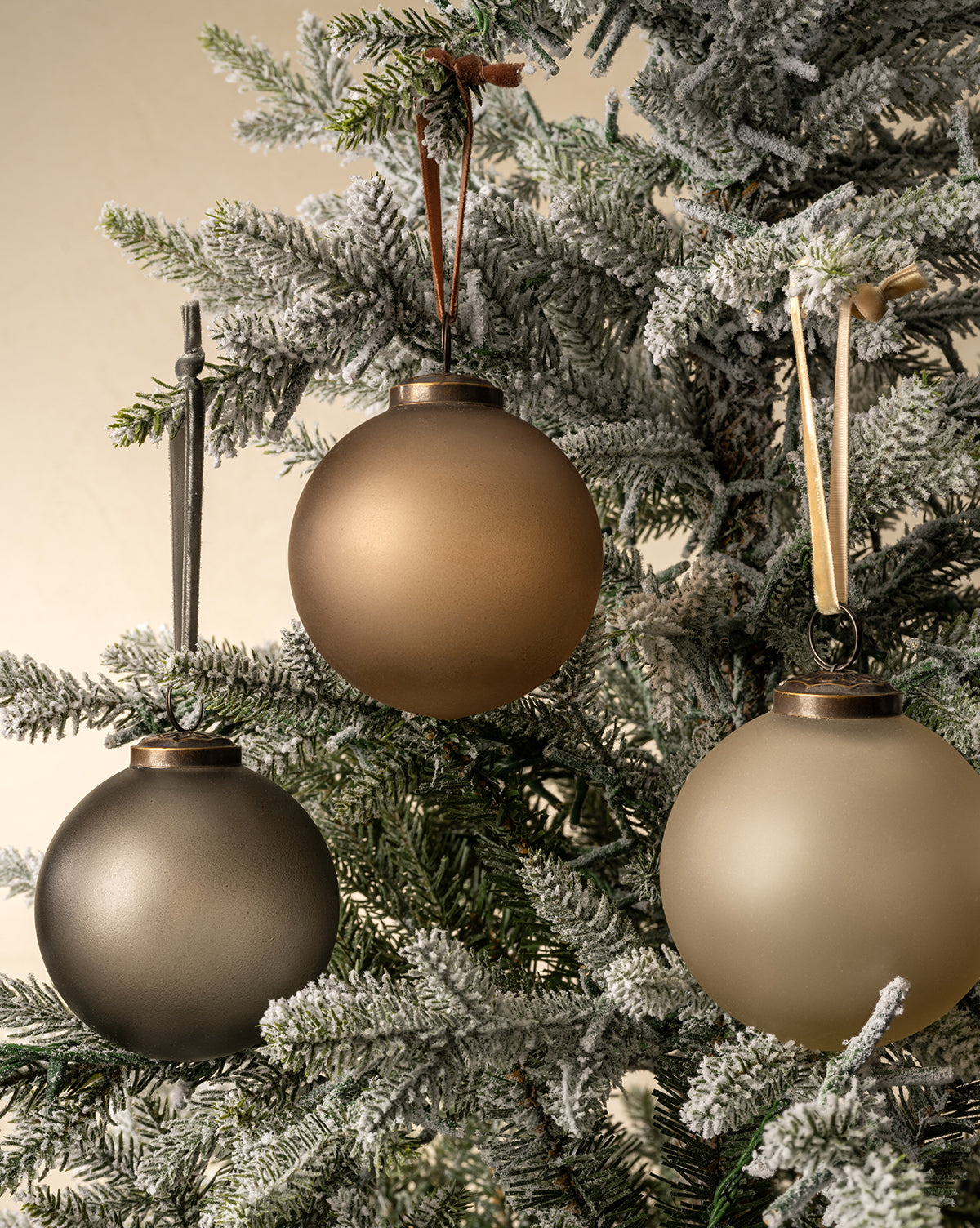 The Noel Neutral Ornaments (Set of 9) feature matte, round gold, bronze, and dark gray baubles with ribbon loops, adding a simple and elegant touch to your snow-dusted artificial pine tree, by Vendixs