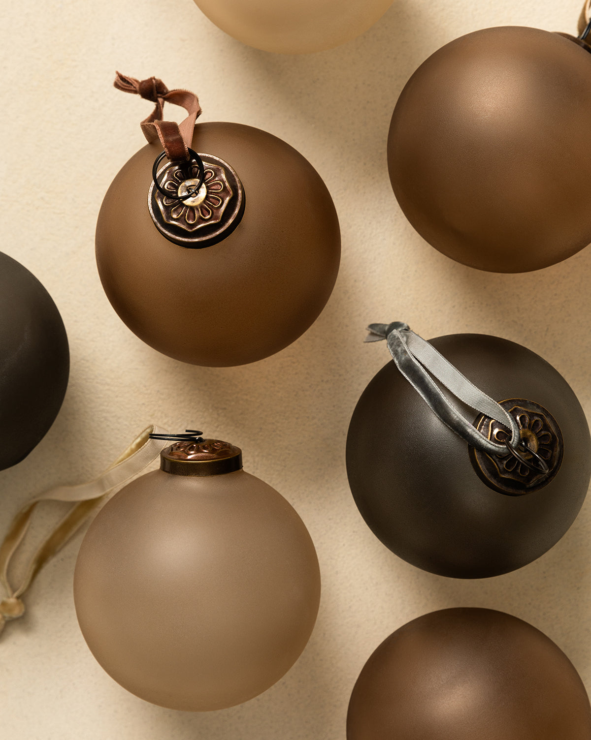 The Noel Neutral Ornaments (Set of 9) feature matte glass baubles in brown and beige, each adorned with velvet ribbons and metallic floral caps—ideal for adding stylish, neutral elegance to your Christmas tree, by Vendixs