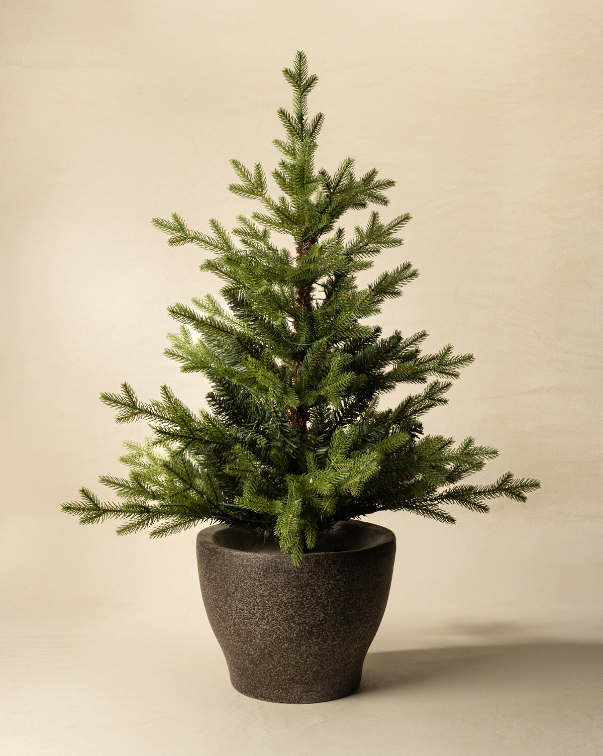 The 3' Norway Pre-Lit Faux Potted Tree features green foliage in a dark, textured ceramic pot and is displayed against a plain beige background, by Vendixs