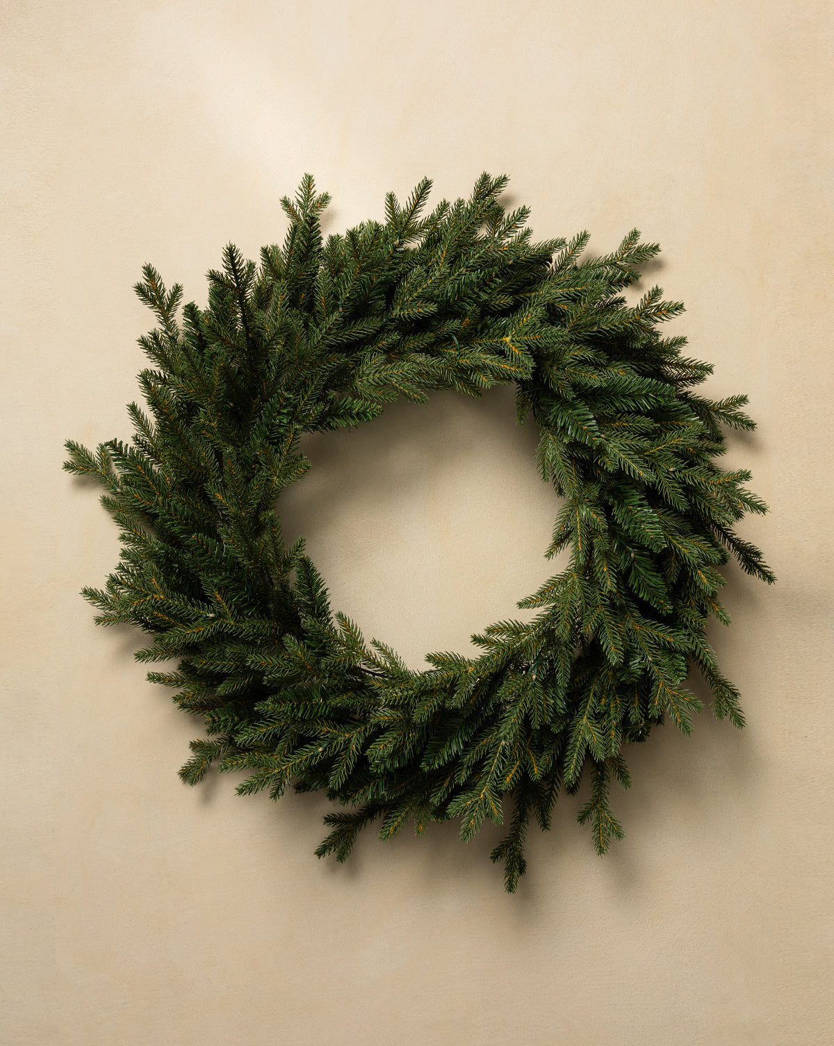 The 20" Norway Pre-Lit Indoor/Outdoor Faux Wreath, featuring dense, lifelike greenery, hangs on a plain beige wall for an elegant holiday accent, by Vendixs
