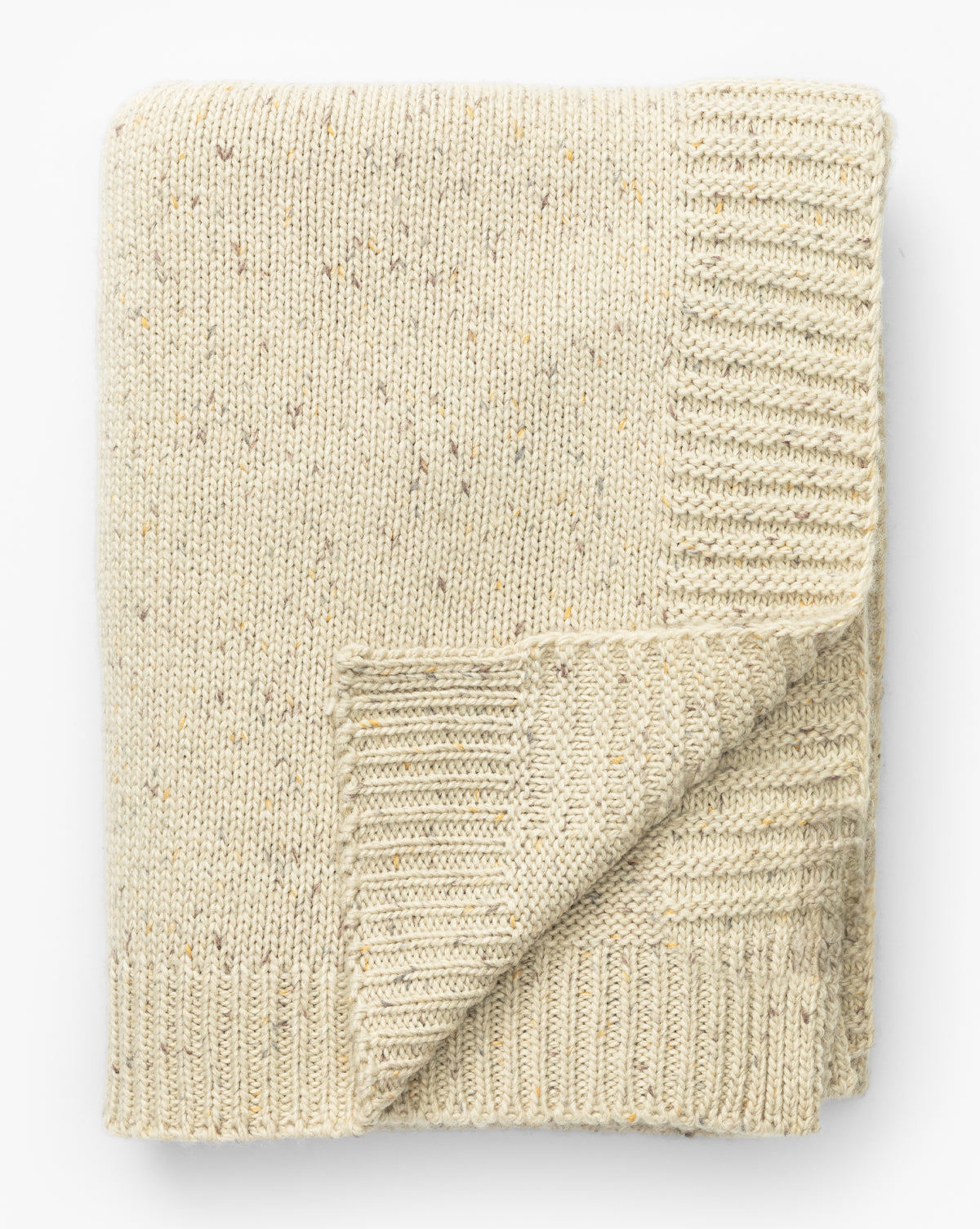 The Otis Knit Throw by Makerspalm is a cozy wool-blend beige throw with grey-speckled fibers and ribbed edges, shown folded on a white background, Vendixs