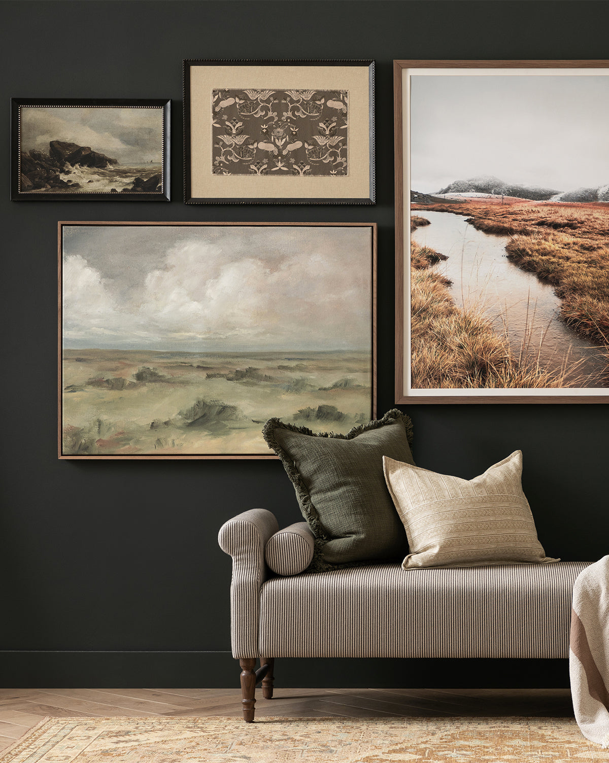 A neutral-toned bench with two throw pillows sits against a dark wall, decorated with four framed Overlook museum-quality wall art pieces in various sizes and earthy tones, by Vendixs