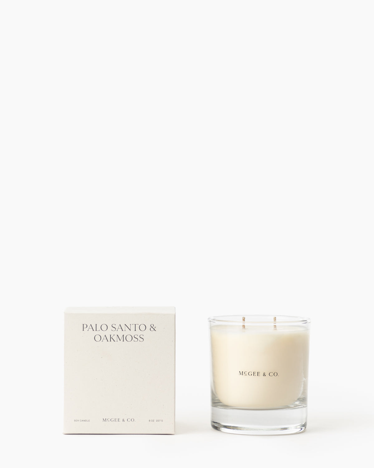 A white box labeled Palo Santo & Oakmoss Candle stands beside a glass luxury soy candle with two wicks, both displaying minimalist Vendixs branding on a white background, by Vendixs