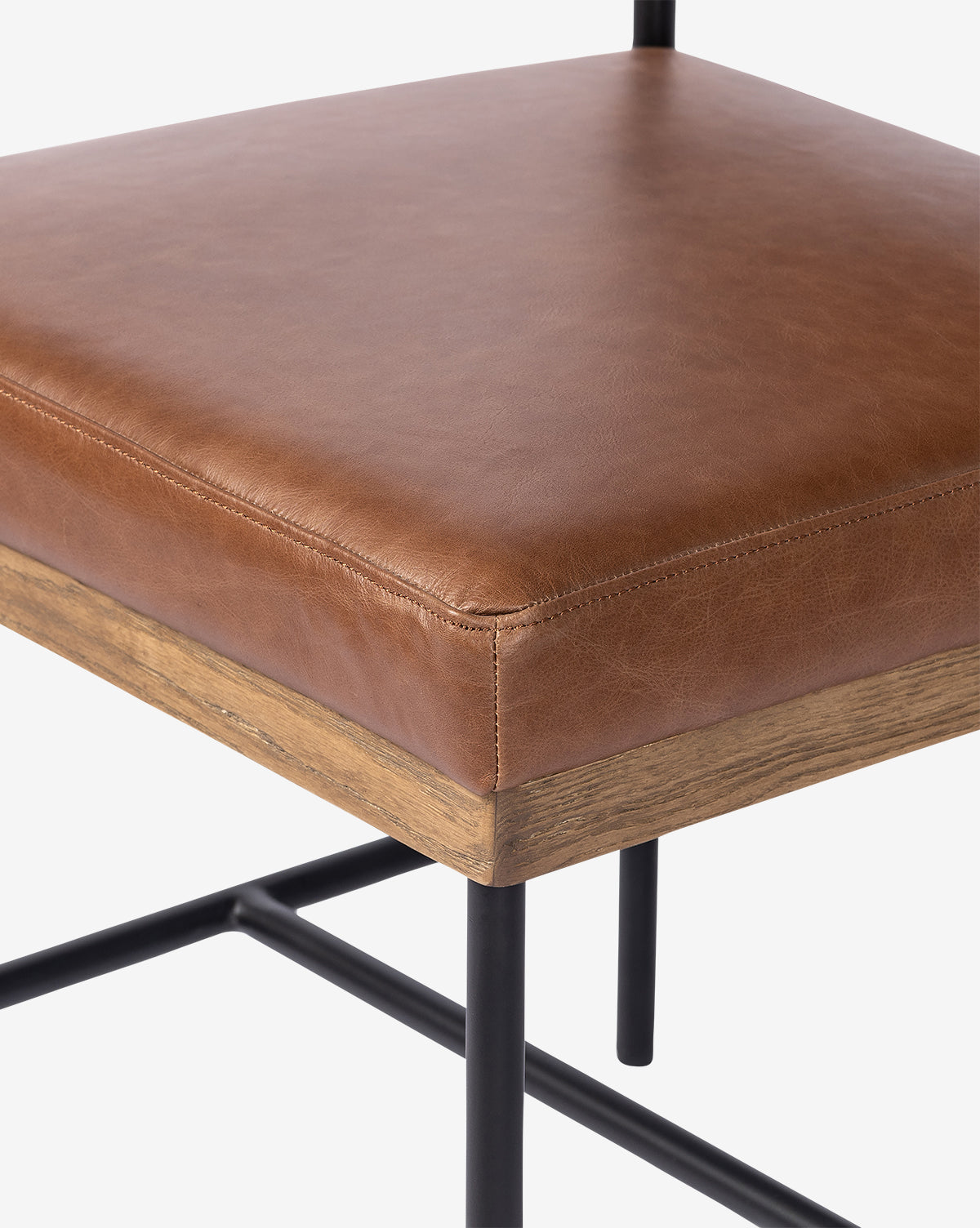 Close-up of the Pascal Dining Chair with a brown leather cushioned seat, wooden trim, and black steel and wood legs with a crossbar—an ideal addition to any dining table setting, by Vendixs