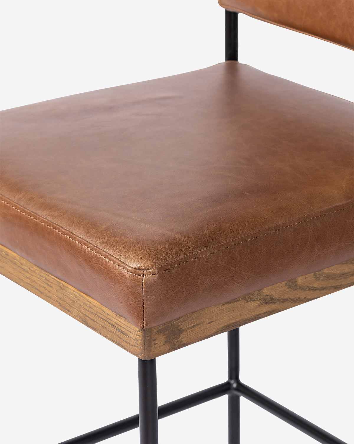Close-up of the Pascal Stool seat with brown leather upholstery, wooden trim at the base, and a black iron frame. This versatile stool features a modern industrial design, by Vendixs
