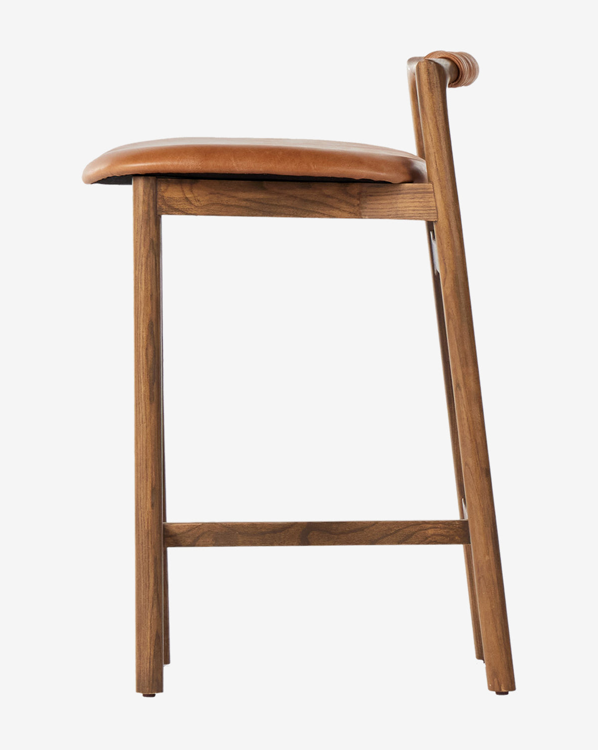 A side view of the Four Hands Patrin Stool, featuring a performance upholstered seat and ash wood frame, displays its modern, minimalist design against a plain white background. Vendixs