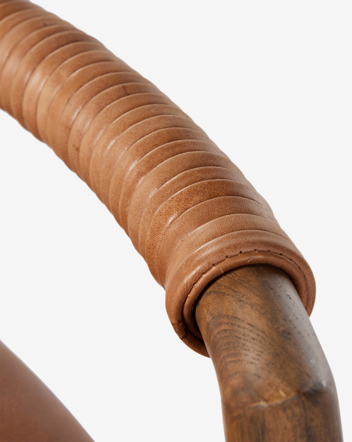 Close-up of a Four Hands Patrin Stool’s ash wood frame armrest, wrapped in smooth light brown leather strips with detailed stitching and texture, set against a plain white background. Vendixs