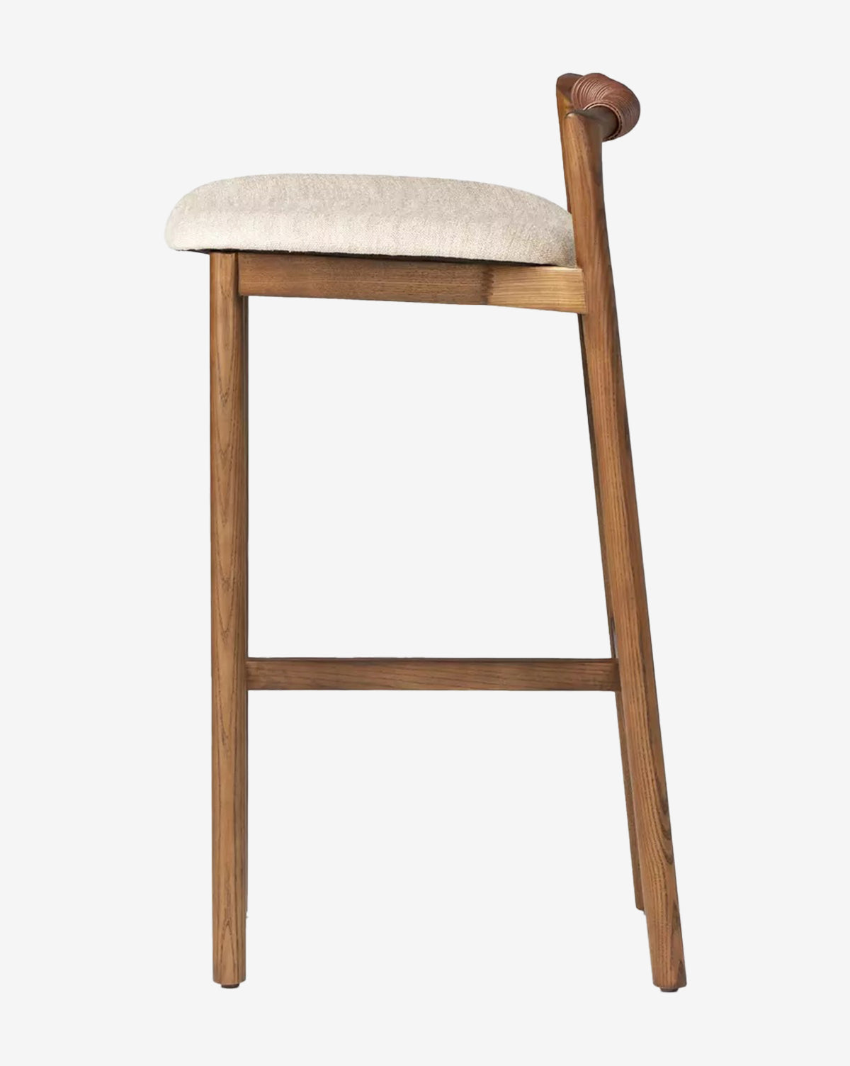 The Four Hands Patrin Stool features an ash wood frame, light beige performance upholstery, and a low curved backrest, shown in profile against a plain white background. Vendixs