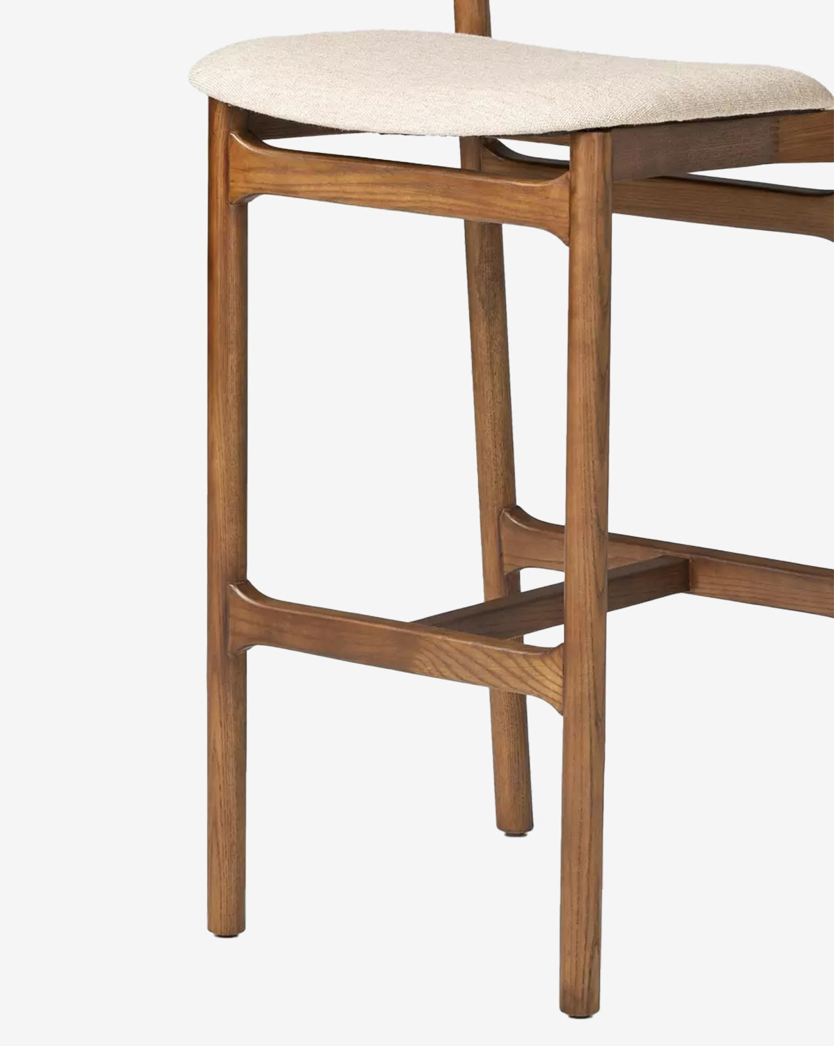 A close-up of the Four Hands Patrin Stool shows its ash wood frame and beige performance-upholstered seat, featuring a mid-century modern design with smooth, rounded edges and visible joinery. Vendixs