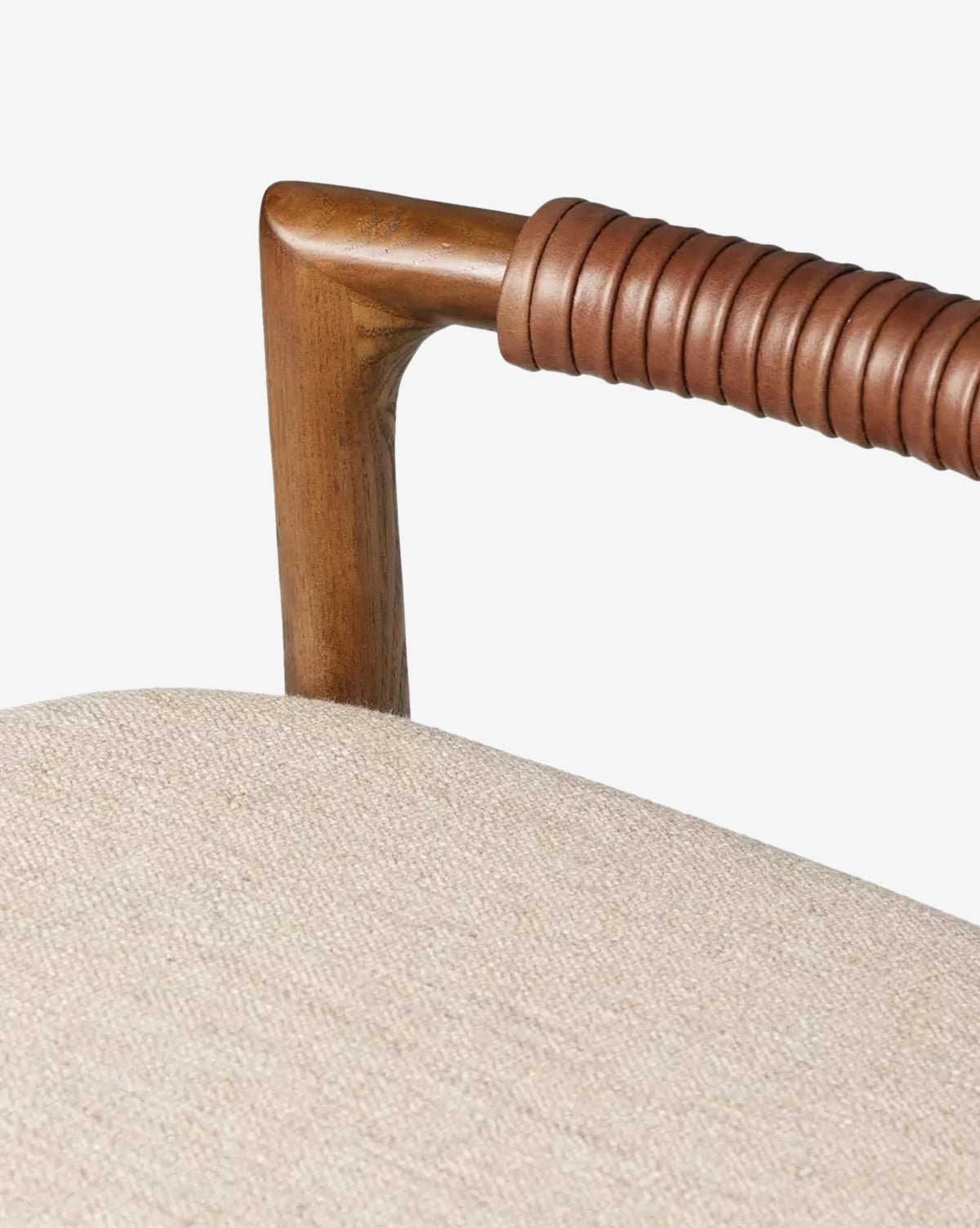 Close-up of a Four Hands Patrin Stool’s ash wood armrest, partially wrapped in coiled brown leather, beside a light beige performance-upholstered seat cushion. Vendixs