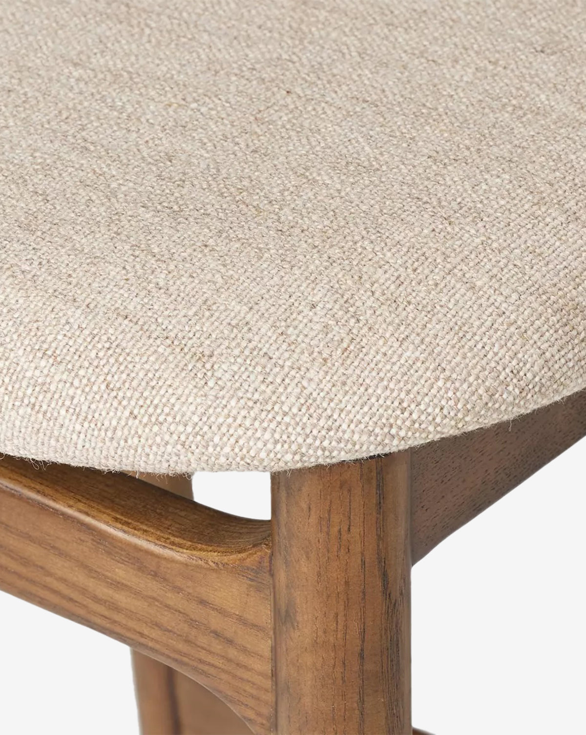 Close-up of the Four Hands Patrin Stool, featuring its performance-upholstered seat in beige woven fabric and displaying the ash wood frame and leg beneath. Vendixs