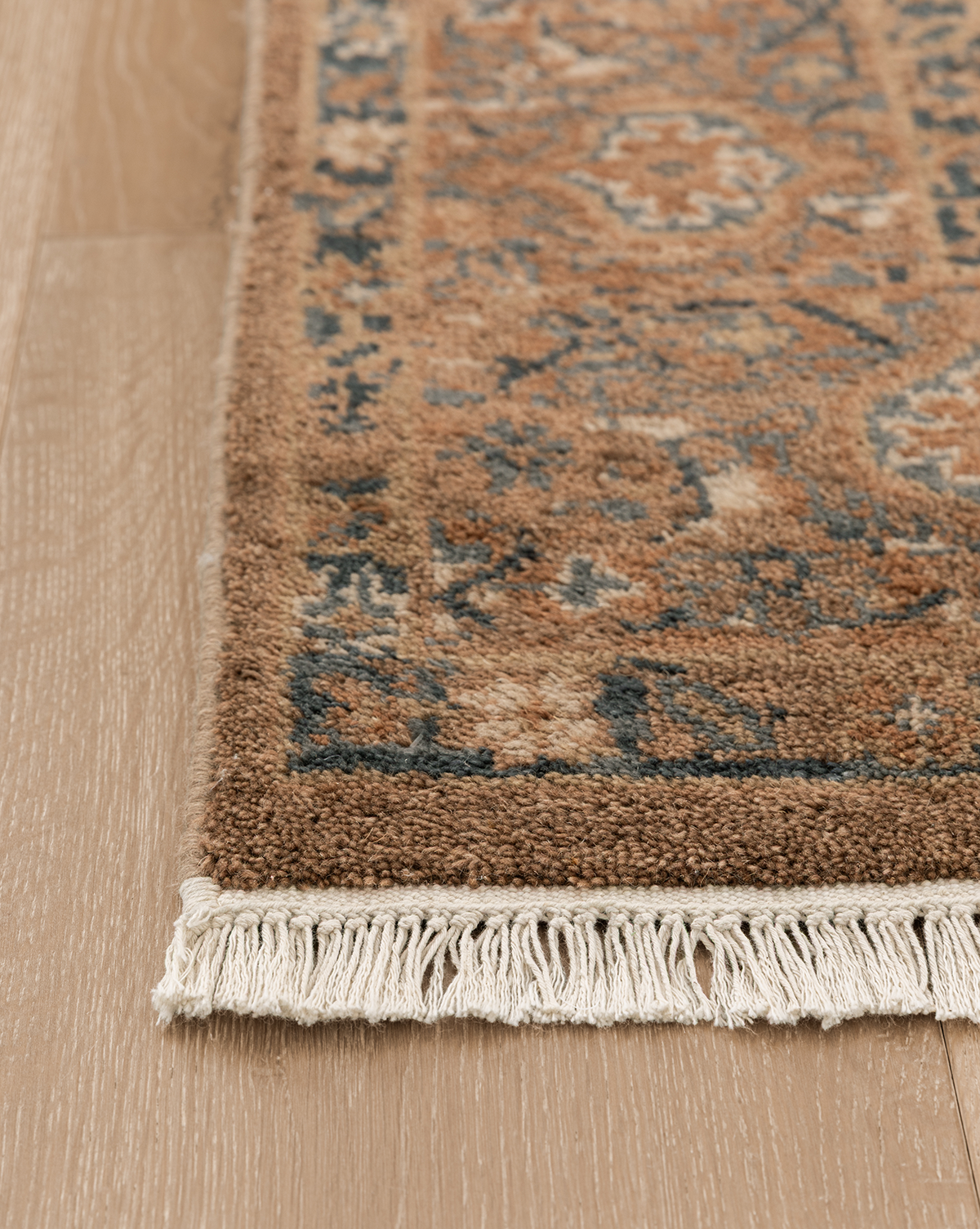 A close-up of the Piedmont Hand-Knotted Wool Rug highlights its blue and brown patterns, beige fringe, and artisanal details, beautifully displayed on a light wood floor, by Vendixs