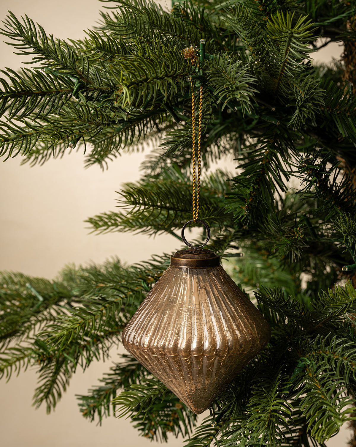 The Piper Ornament, a ribbed glass diamond hanging from a green Christmas tree branch by a gold string, adds elegant metallic style to your festive decor, by Vendixs