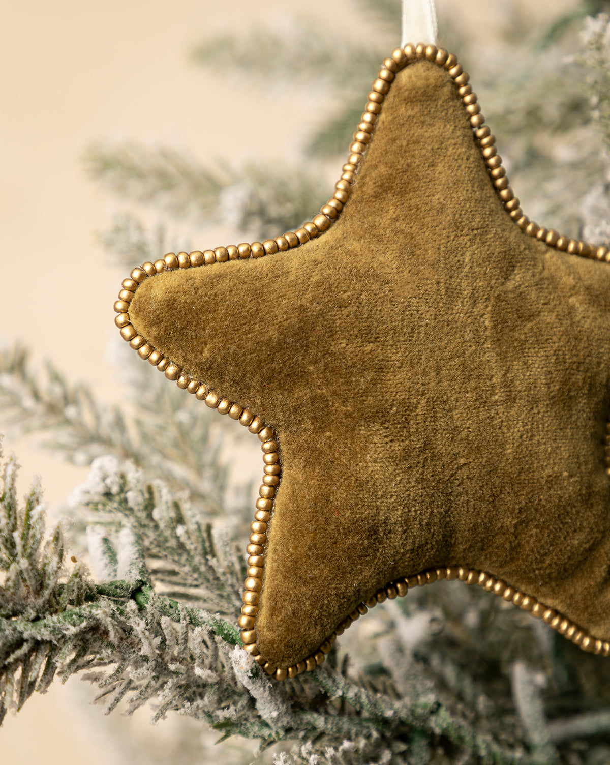 A close-up of the Plush Beaded Star Ornament showcases its beaded edges and festive style as it hangs from a frosted holiday tree branch, by Vendixs