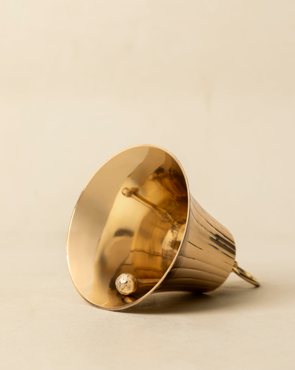 The Polished Brass Bell rests on a neutral surface, displaying its clapper and simple loop handle—ideal for adding vintage-inspired charm to your holiday décor, by Vendixs
