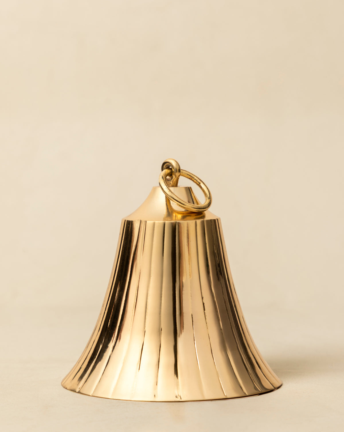 The Polished Brass Bell features vertical ridges and a loop handle, with a shiny gold finish that adds vintage-inspired elegance to holiday decor, especially when displayed against a plain, light background, by Vendixs