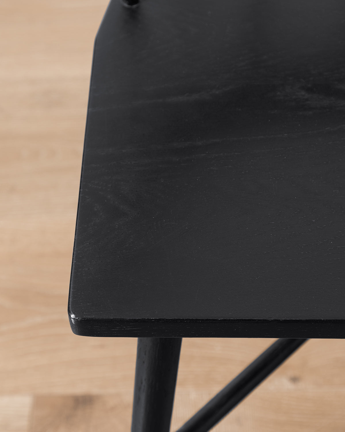 Close-up of a black wooden table corner with a smooth surface, positioned near the sleek Reeves Dining Chair on a light wood floor, highlighting the table’s edge and leg details, by Vendixs