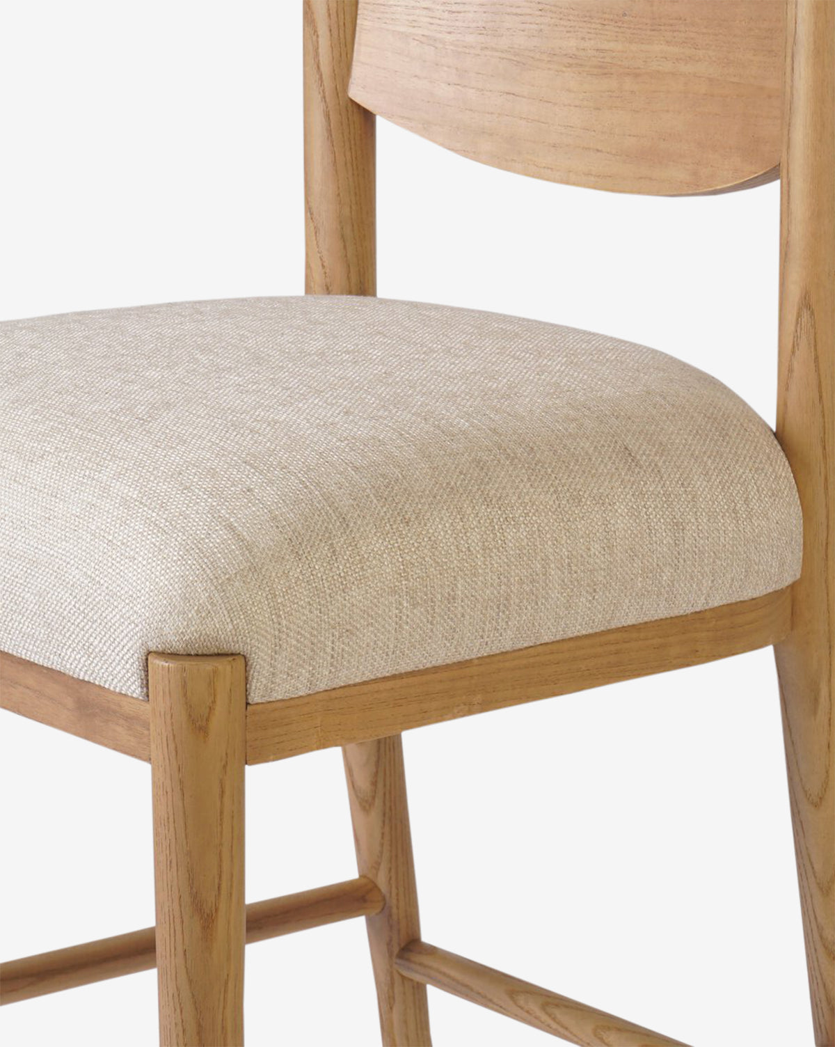 Close-up of the Four Hands Reverie Stool, showcasing its natural wood frame, light beige upholstered seat, and curved backrest—an ideal modern kitchen accent—set against a plain white background. Vendixs