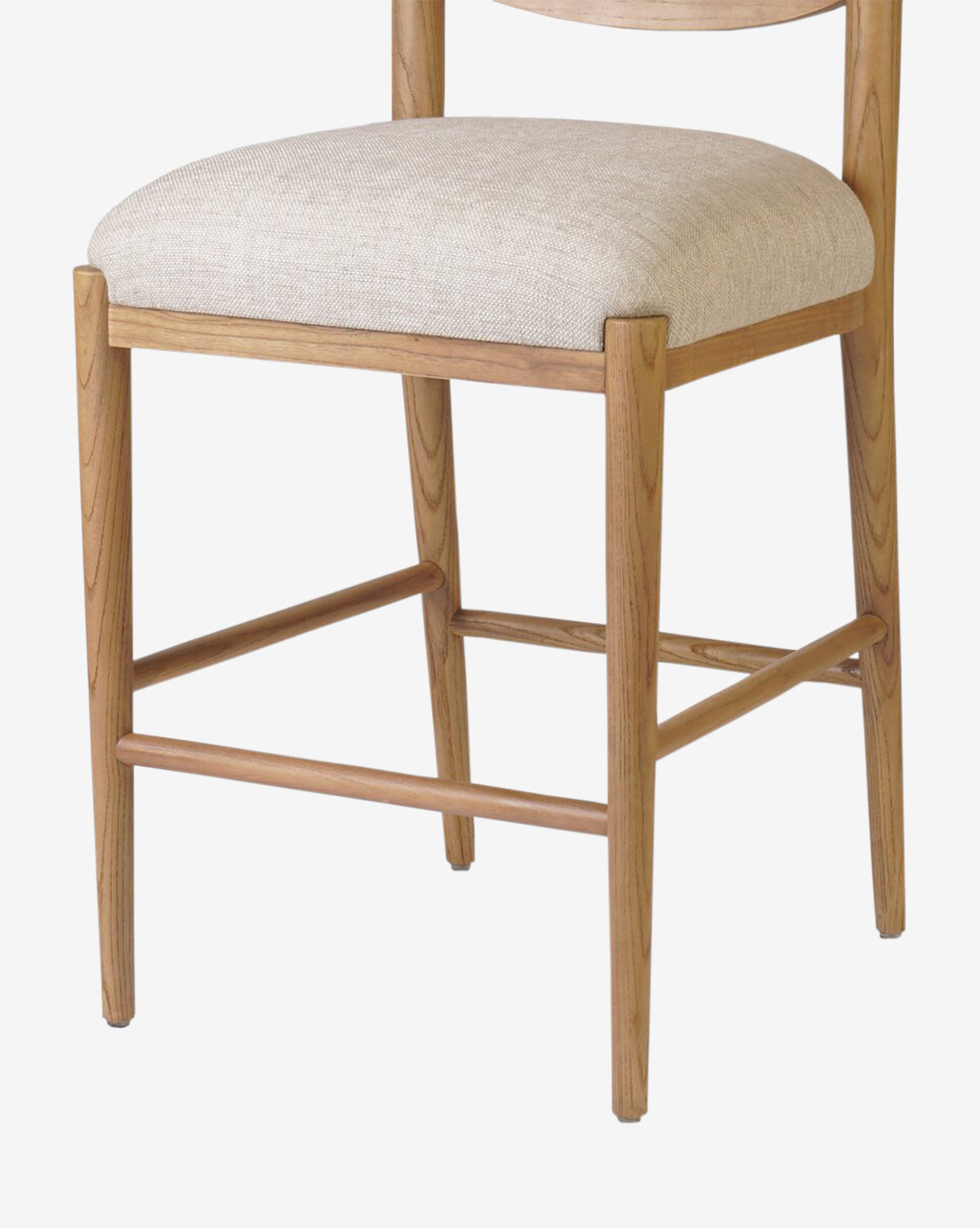 The Four Hands Reverie Stool features natural light brown wood legs and a beige upholstered seat, shown from a front-side angle—ideal for bringing warmth to your kitchen space. Vendixs
