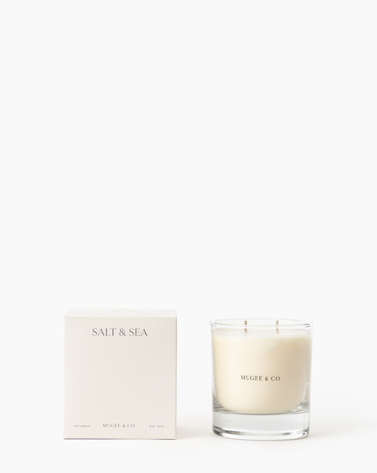 A minimalist white soy wax Salt & Sea Candle in a clear jar sits beside its box, both labeled and displayed against a plain white background, by Vendixs