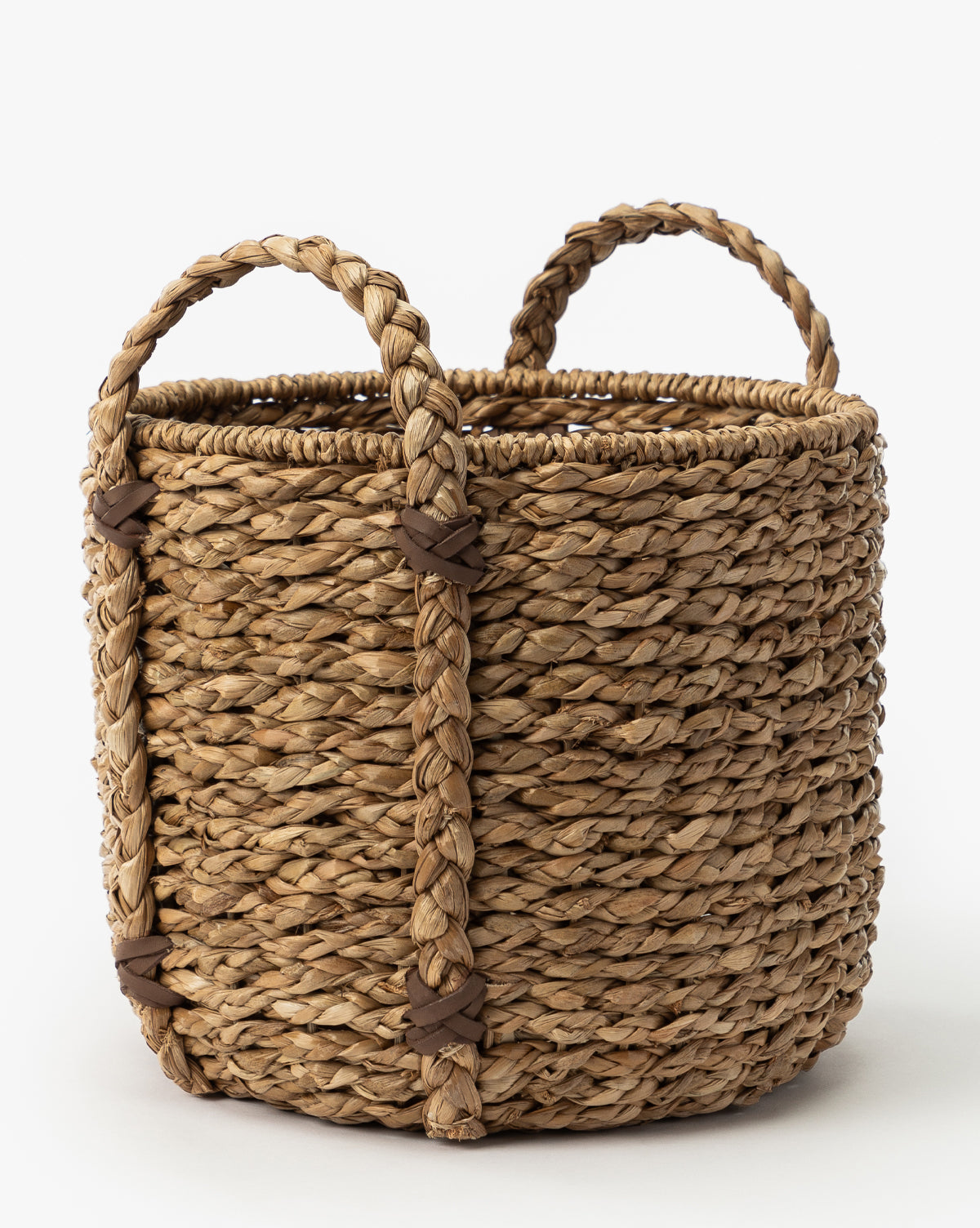The Salter Woven Basket is a round seagrass basket made from natural fibers, featuring two braided handles with brown leather-like bands, shown on a white background by Vendixs