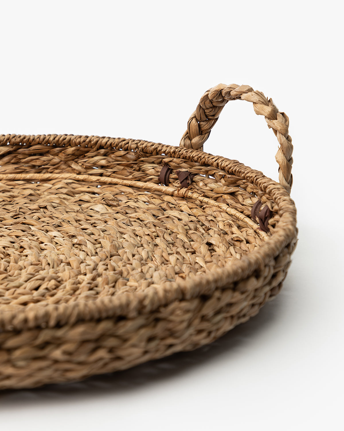 A close-up of the Salter Woven Tray, a round straw storage tray with a braided handle, displayed on a white background, by Vendixs